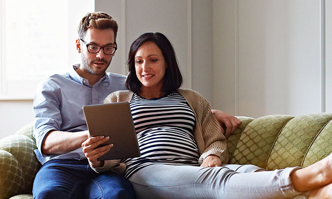 Husband and wife sitting on couch with tablet.