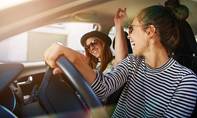 Two women in a car dancing to music.