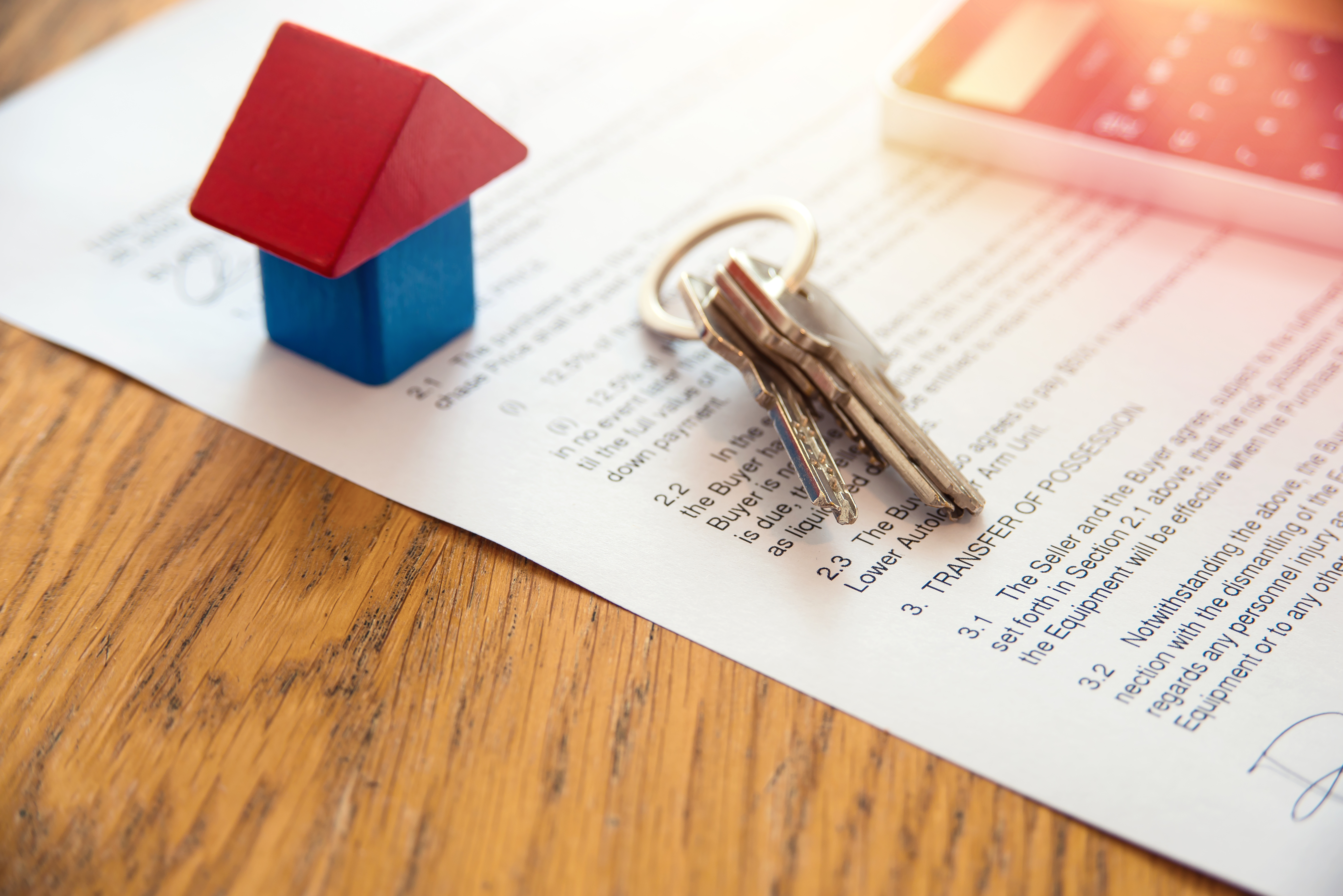 Photograph of a toy house and house keys lying on a home closing document.